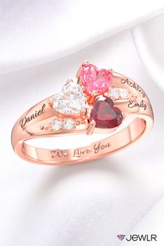 two hearts with names engraved on the side and three stones in each ring, set against a white satin background