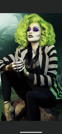 a woman with green hair and makeup sitting on a rock