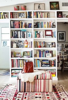 a living room filled with lots of books on top of a white book shelf next to a window