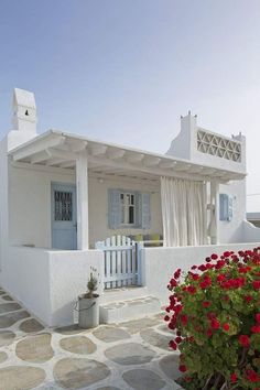 a white house with red flowers in front of it and a blue door on the side