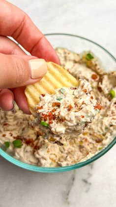 a hand holding a cracker over a bowl of dip