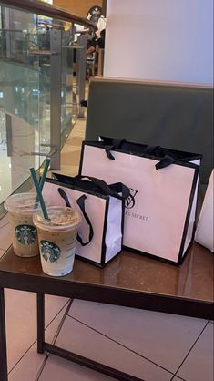 two starbucks bags sitting next to each other on a table with drinks in front of them