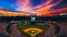 a baseball stadium filled with lots of people watching the sun go down over the field