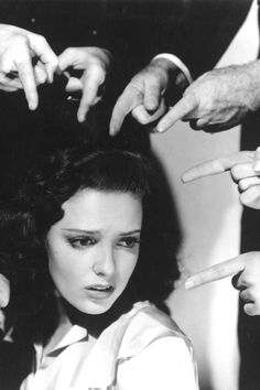 black and white photograph of a woman getting her hair done by several people holding their hands up