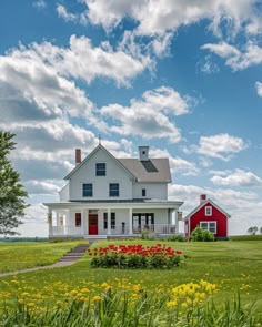 a red and white house sitting on top of a lush green field next to flowers