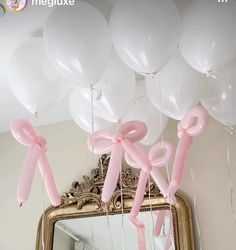 white balloons with pink bows are hanging from a mirror in front of a gold frame