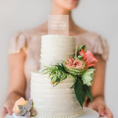 a woman holding a white wedding cake with flowers on it and a sign that says welcome to the bride