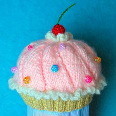 a knitted cupcake ornament with a cherry on top, sitting on a blue background