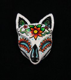 a white mask with red and green designs on it's face, against a black background