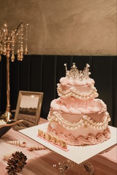 a three tiered pink cake on top of a table with pine cones and candles