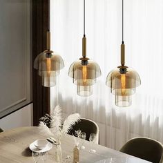 three lights hanging over a dining room table with plates and glasses on top of it