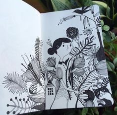 an open book with black and white drawings on it next to some green plant life