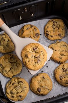 a spatula scooping chocolate chip cookies out of an air fryer to bake