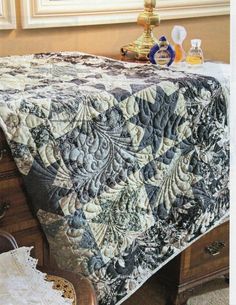 a bed with a quilt on top of it next to a lamp and dresser in a room