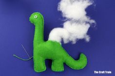 a green toy dinosaur sitting on top of a blue surface next to white fluffy clouds