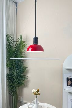 a red light hanging over a table with a white vase and flower in front of it