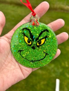 a hand holding a green ornament with a grin face on it's face