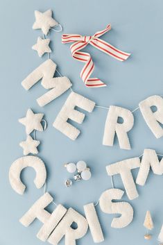 the word merry christmas spelled out with felt stars and ribbons on a blue background next to other letters