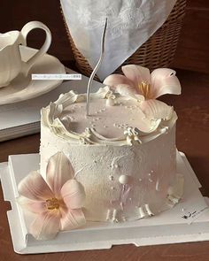 a white cake with pink flowers and a teapot on the table next to it