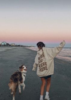 a woman and her dog walking on the beach at sunset with their arms in the air