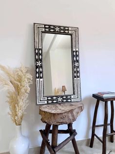 a mirror sitting on top of a wooden stool next to a vase with flowers in it