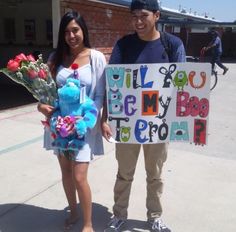 two people standing next to each other holding flowers and a sign that says will you be my hero?