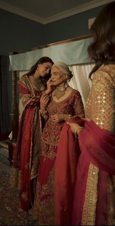 two women dressed in red and gold standing next to each other with their arms around one another