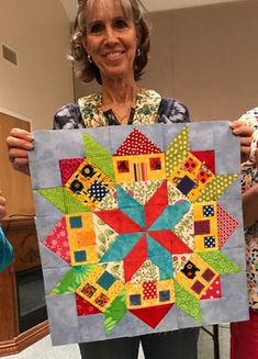 an older woman holding up a colorful quilt