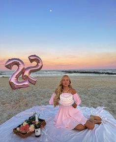 a woman sitting on top of a blanket holding a cake in front of the ocean