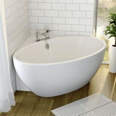 a white bath tub sitting next to a window in a bathroom with wooden flooring