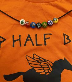 an orange shirt with a black horse and seven colorful beads hanging from it's chest