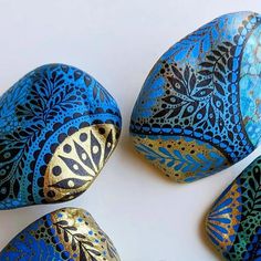 three blue and gold painted rocks on a white surface