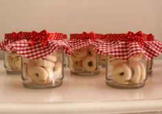 four glass jars filled with small stuffed animals in red and white bows on top of a table