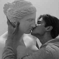 a man and woman kissing in front of a statue