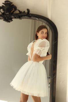 a woman is standing in front of a mirror wearing a short white dress and heels