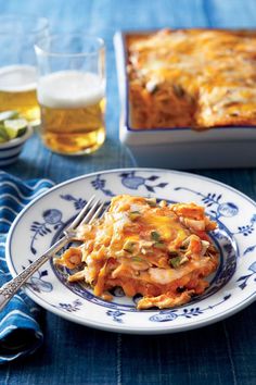 a blue and white plate topped with lasagna next to a glass of beer