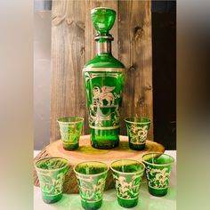 a green glass set on top of a wooden table next to glasses and a bottle