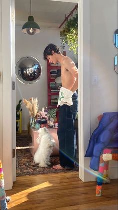 a man standing in front of a mirror next to a white dog on a wooden floor