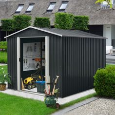 a black shed sitting on top of a lush green field next to a building with lots of windows