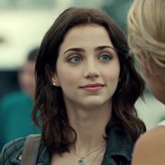 a woman with blue eyes is talking to another woman in a black leather jacket and necklace