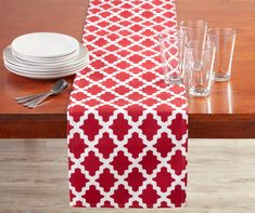 a red and white table runner on top of a wooden table with plates and glasses