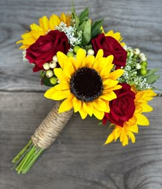 a bouquet of sunflowers and red roses on a wooden table with other flowers