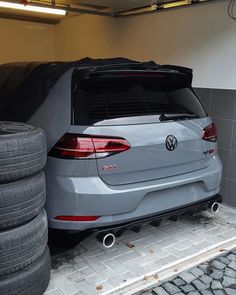 the back end of a gray car parked in a garage with several tires on the ground