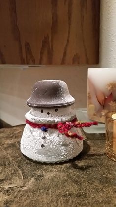 a small snowman sitting on top of a table next to a candle