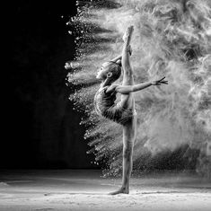 a ballerina in black and white kicking up dust from her arms while standing on one leg