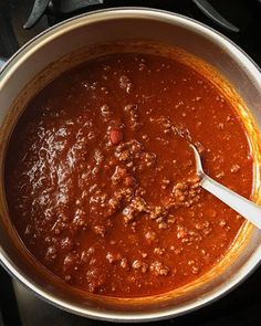 a pot full of chili on top of a stove with a ladle in it