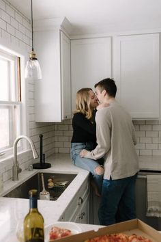 a man and woman standing next to each other in a kitchen with pizza on the counter