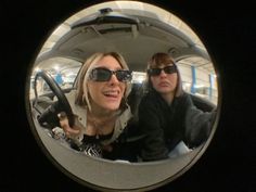 two women are sitting in the back seat of a car and one is holding a steering wheel