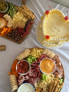 two platters filled with cheese, crackers and dips next to a heart shaped cake