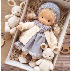 a doll and two stuffed animals in a box on a wooden table with straw grass